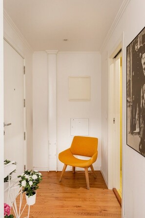 Ein Korridor mit Holzboden, einer weißen Tür, einem gelben Stuhl und einem gerahmten Bild an der Wand.