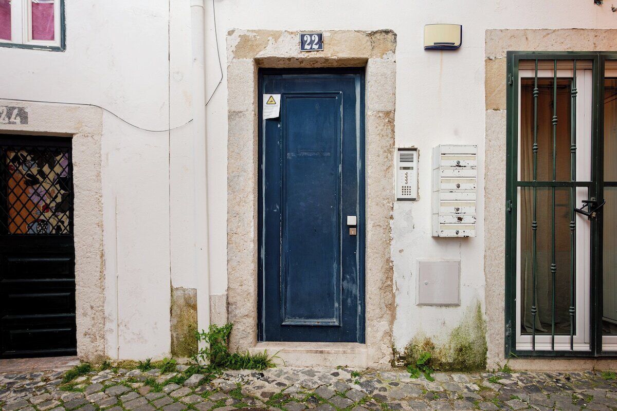 Un edificio con una puerta azul, un letrero con el número 22 arriba y una pequeña ventana con una reja de metal.