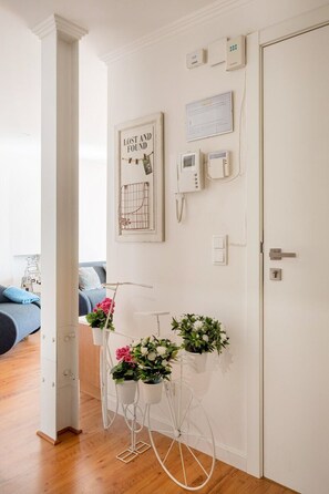 Ein Zimmer mit einer weißen Tür, einem an der Wand befestigten Telefon, einem gerahmten 'LOST AND FOUND' Schild und einem weißen Wagen mit Blumen.