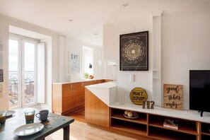 A modern kitchen with a dining area, a TV, and a wall with decorative items. - Alfama River Light | Sunlit Views & AC (Lisbon)