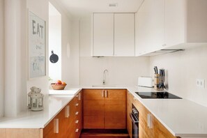 A modern kitchen with white cabinetry, a black stove, and a white countertop. - Alfama River Light | Sunlit Views & AC (Lisbon)