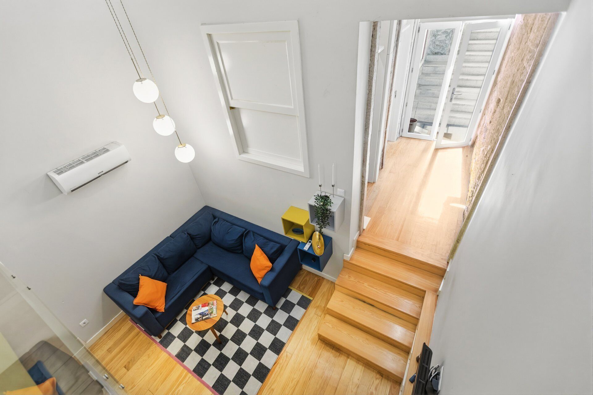 Un salon moderne avec un canapé bleu, un tapis à carreaux et un escalier menant à l’étage supérieur.