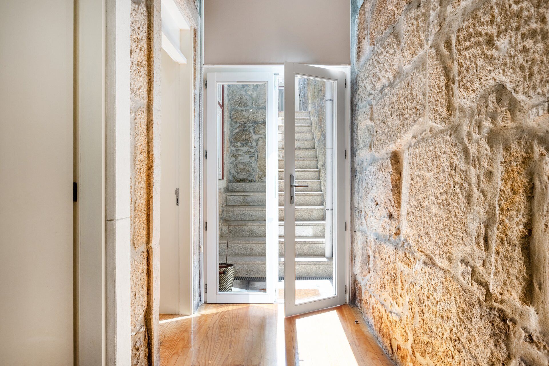 A hallway with a stone wall, a wooden floor, and a door leading to a staircase.