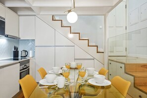 A modern kitchen with a dining area, a staircase, and a glass table set for a meal. - Recanto do Porto with Private Patio and AC (Porto)