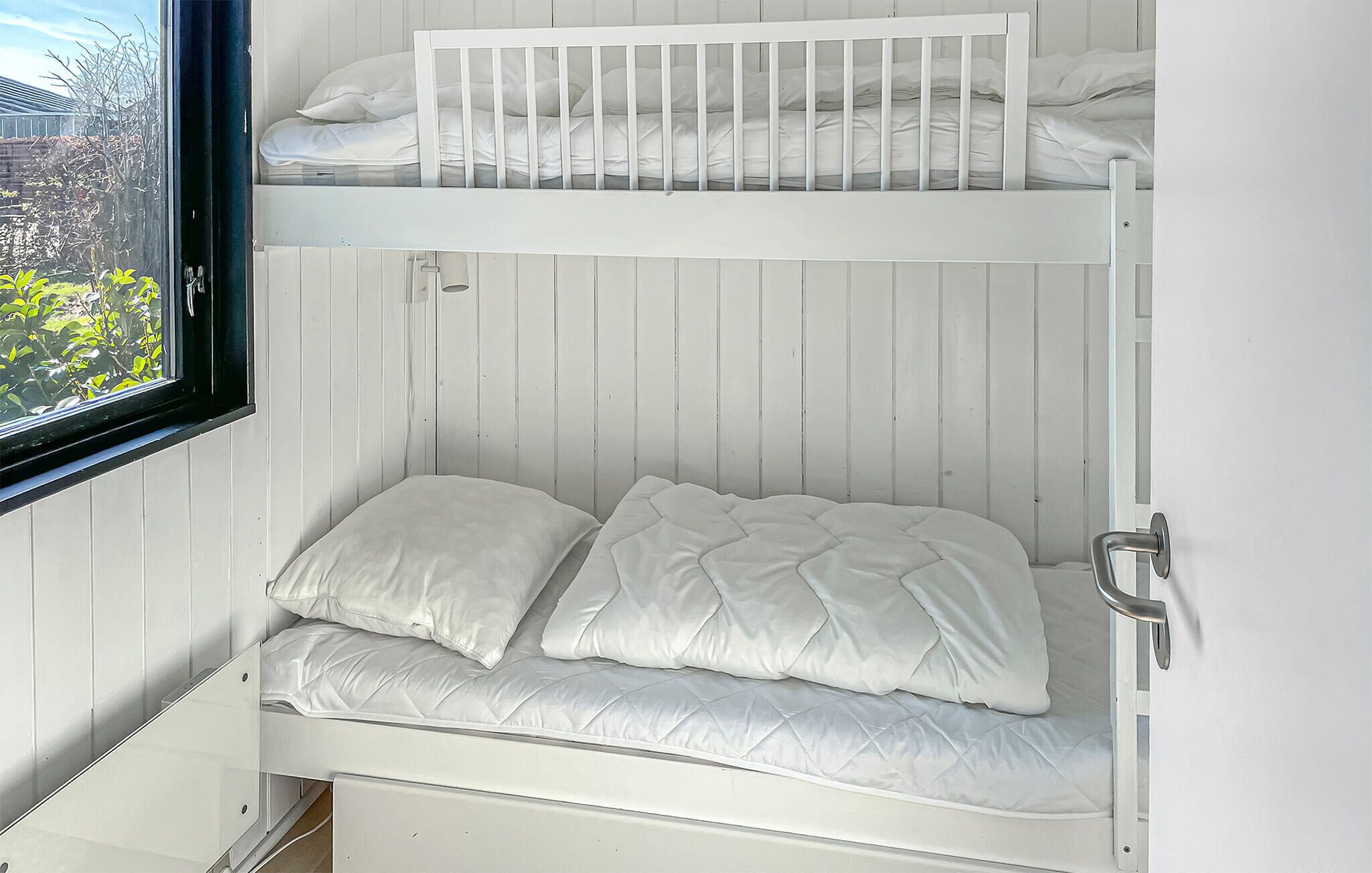A bunk bed with white bedding and a window with a view of greenery.