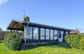 Una casa moderna con un gran ventanal, una chimenea y un porche cubierto.