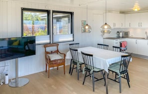 Un comedor con una mesa, sillas, un televisor y una cocina al fondo.