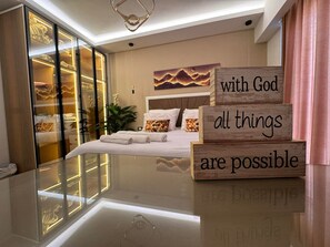 Ein modernes Schlafzimmer mit begehbarem Kleiderschrank mit Glastüren, einem Bett mit weißer Bettwäsche und einem motivierenden Zitat auf Holzblöcken.
