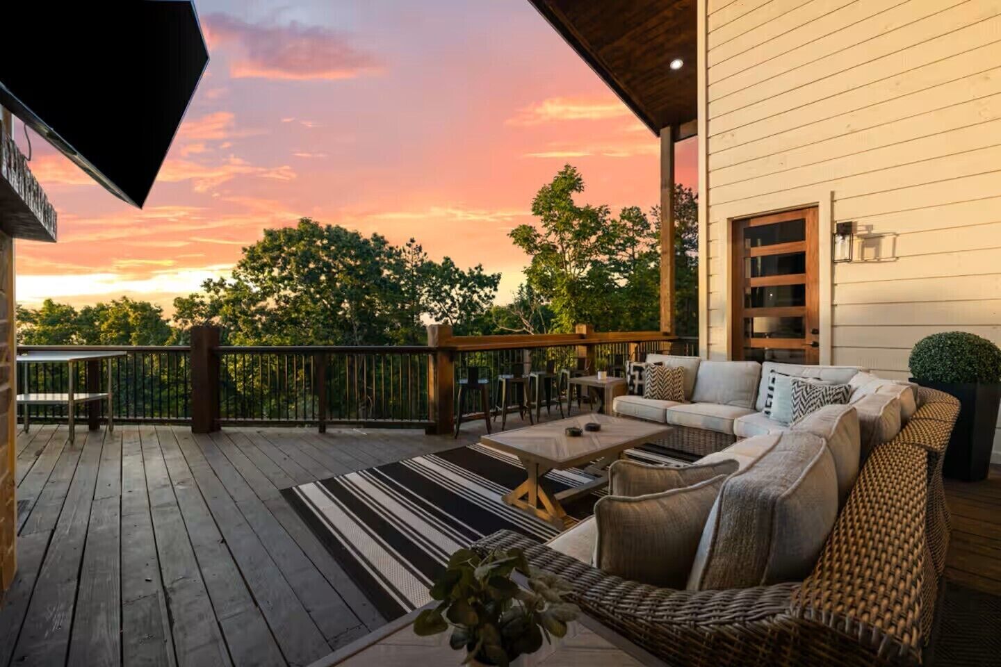 A deck with outdoor furniture, a railing, and a view of trees and sky.