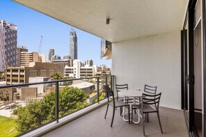 Un balcone con tavolo e sedie, affaccia su uno skyline urbano con diversi edifici.
