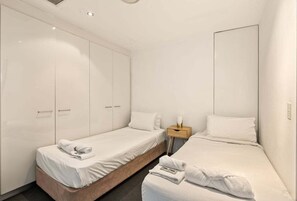 Una camera d'albergo con due letti singoli, un armadio, un comodino e un tavolino di fianco al letto.