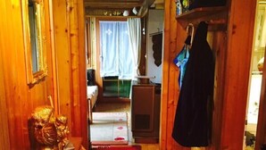 Ein schmaler Korridor mit Holzwänden, einer Bank, einem Kleiderständer und einer Tür zu einem Zimmer mit Bett und Vorhängen.