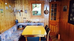 Ein Interieur einer Holzhütte mit Esstisch, Stühlen, einer Bank, einem Fenster und einem Schrank.