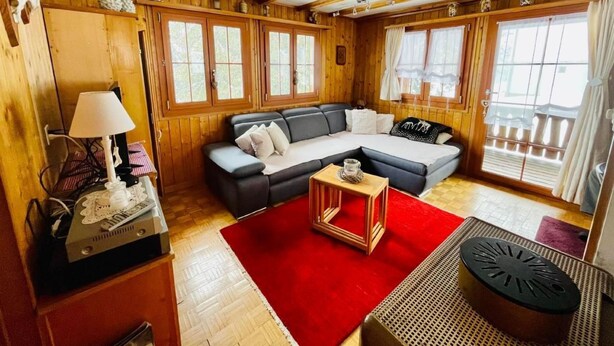 Ein gemütliches Blockhaus-Interieur mit einer Eckcouch, einem kleinen Tisch und einem roten Teppich.