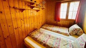 Ein Holzhütten-Zimmer mit einem Bett, Regalen und einem Fenster mit Vorhängen.