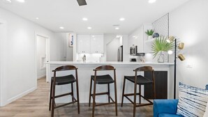 Une cuisine moderne avec des meubles blancs, un îlot central et trois tabourets de bar.