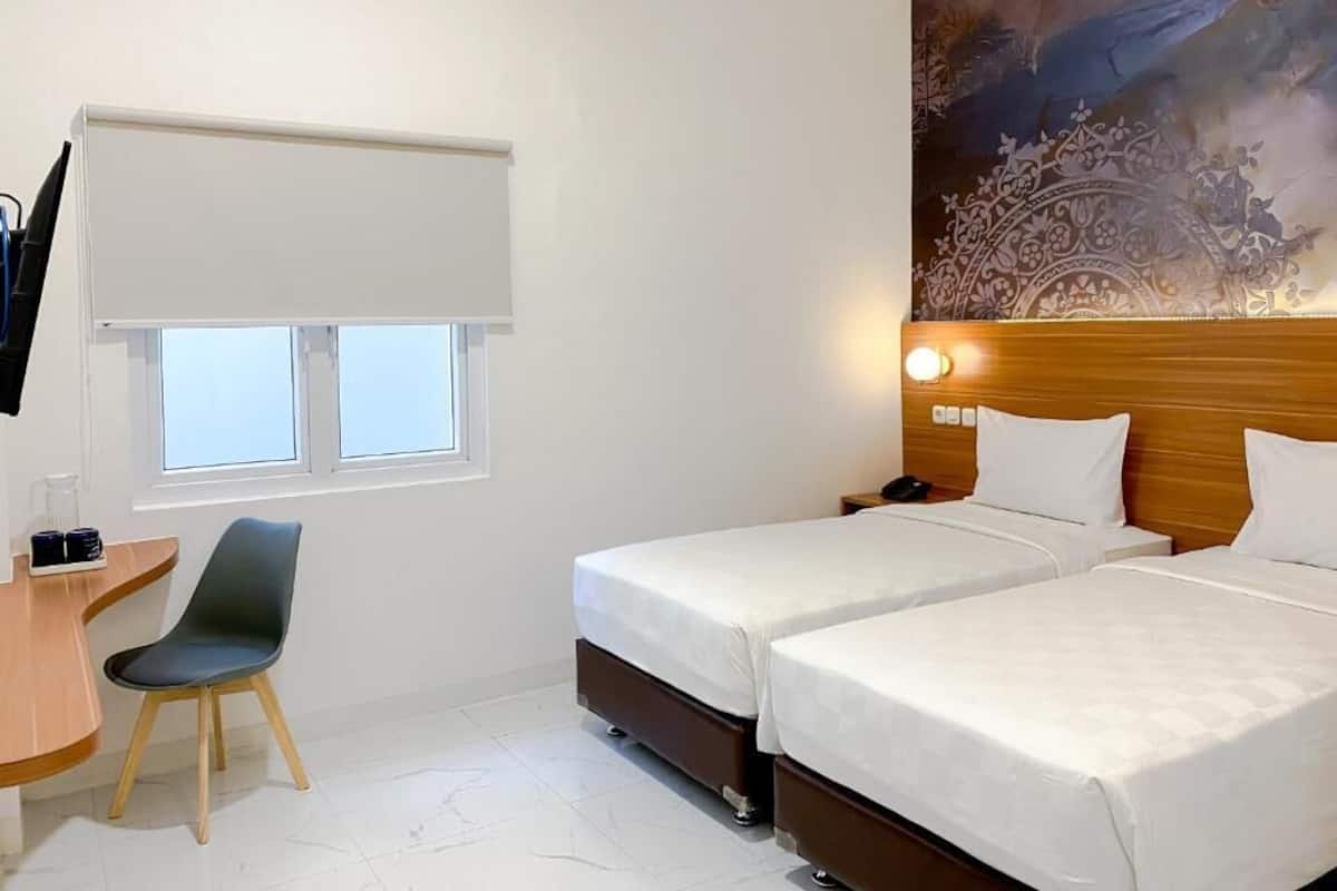 A hotel room with two beds, a desk with a chair, a TV, and a window with a blind.