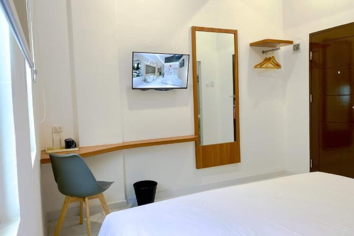 A hotel room with a bed, a desk with a chair, a television, a mirror, and a wardrobe.