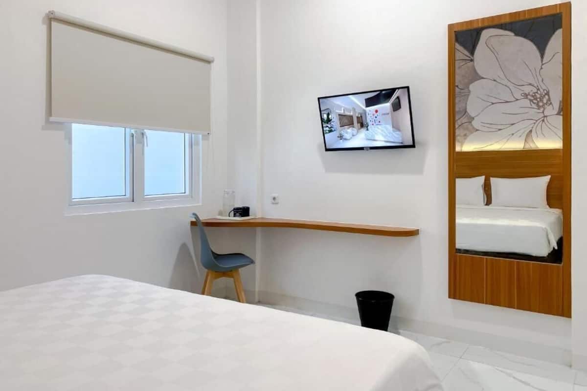 A hotel room with a bed, a desk, a chair, a TV, and a wall-mounted shelf with a bed and a picture.