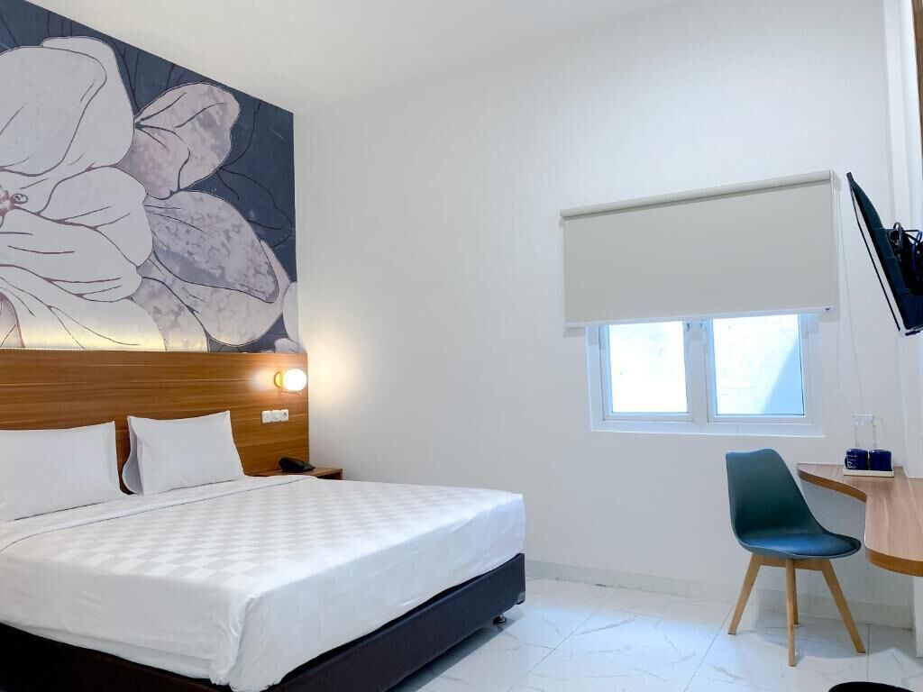 Une chambre d’hôtel comprenant un lit, un bureau avec une chaise, une grande œuvre d’art florale accrochée au mur, une fenêtre avec un store et un téléviseur fixé au mur.