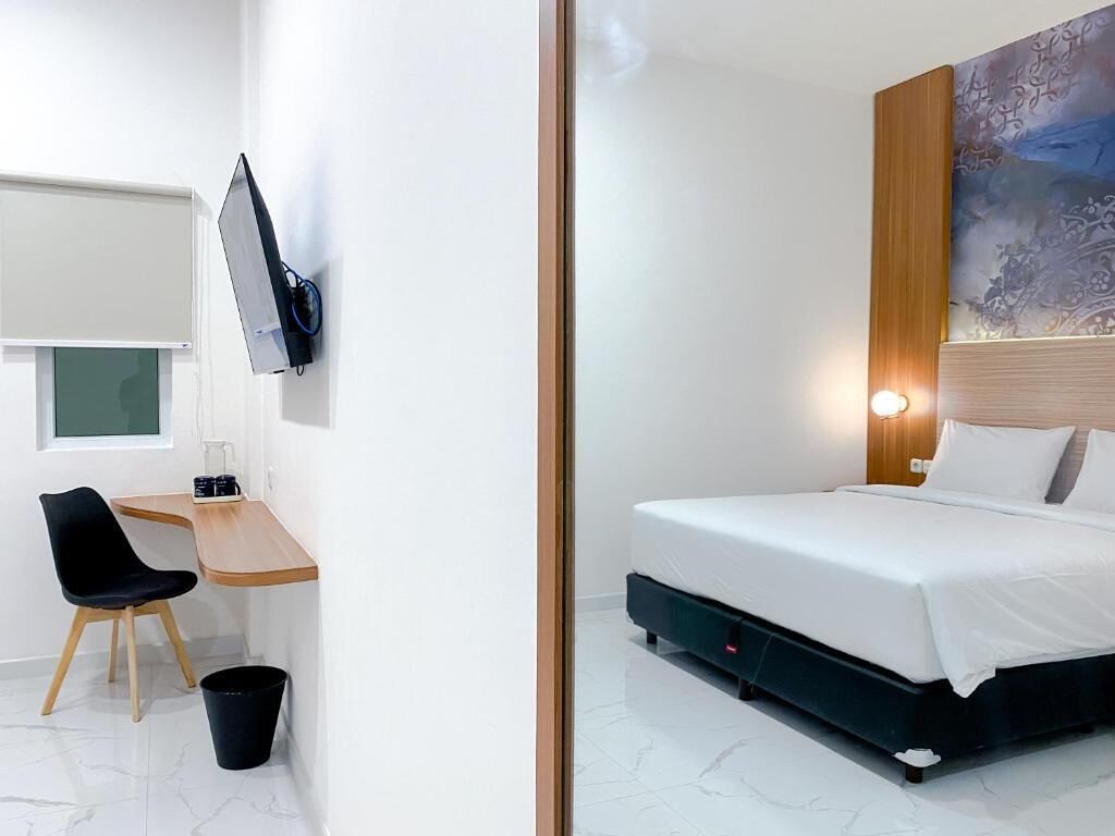 Quarto de hotel com cama, escrivaninha, cadeira, televisão e um quadro na parede.