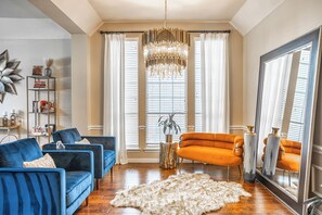 A living room with a chandelier, blue and orange sofas, a white rug, and a large mirror. - The Glam House 10mi from AT&T Stadium (Grapevine)