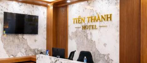 A hotel reception desk with a marble wall, a television, and a wooden reception area.