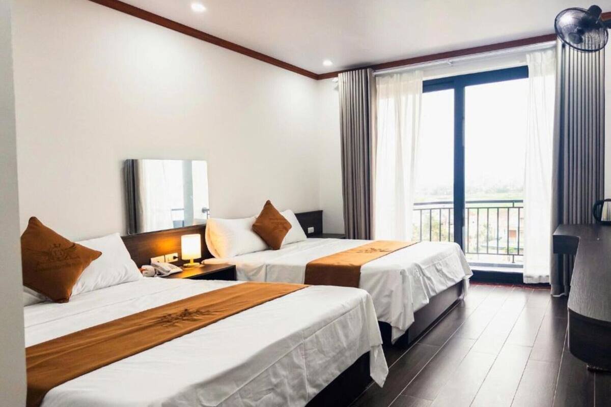 A hotel room with two beds, a desk, a chair, and a large window with curtains.