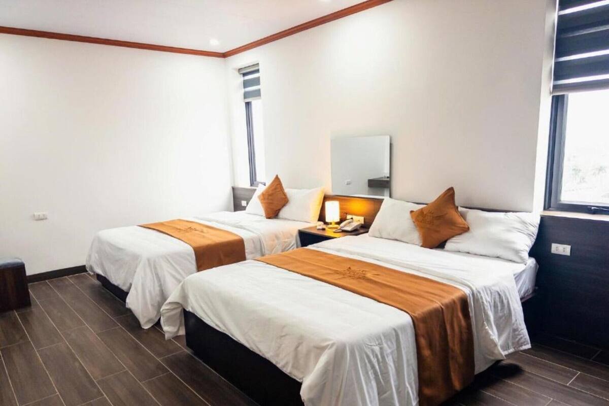 A hotel room with two beds, a nightstand, a lamp, and a window.