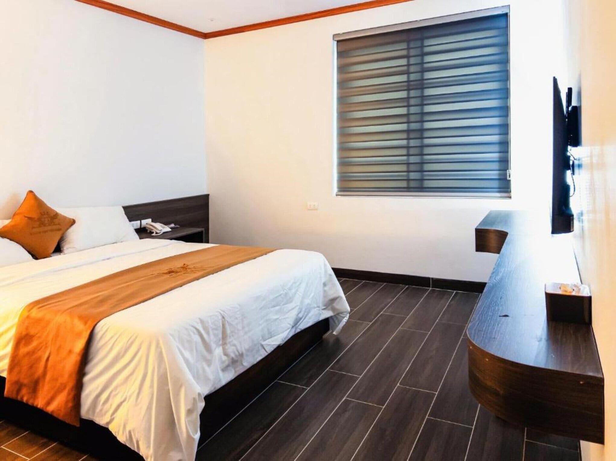 Une chambre d’hôtel avec un lit, une table de chevet, une télévision et une fenêtre avec des stores.