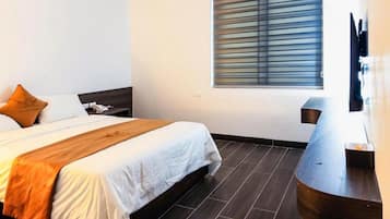 Une chambre d’hôtel avec un lit, une table de chevet, une télévision et une fenêtre avec des stores.