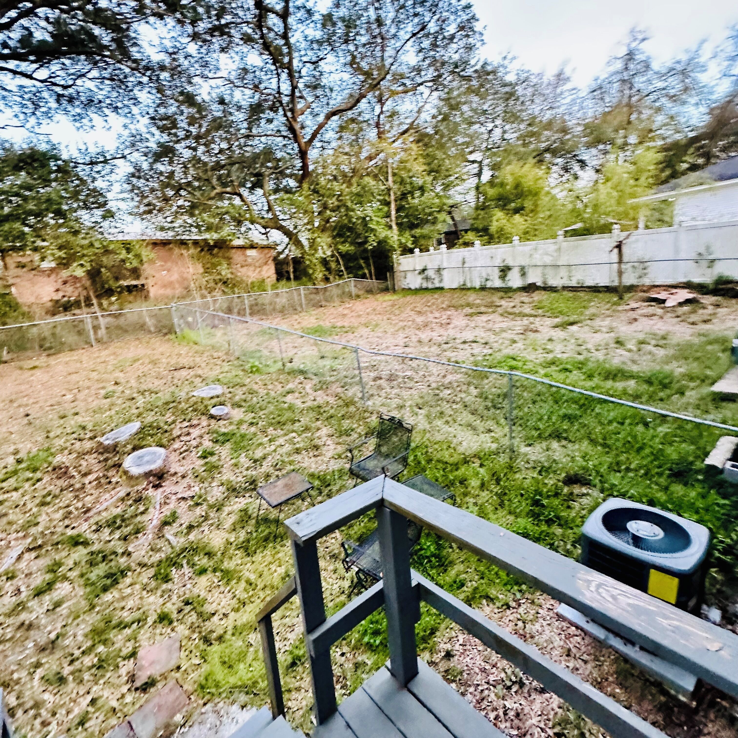 Une cour arrière clôturée, avec une terrasse en bois, un portail en métal et un mur en béton.