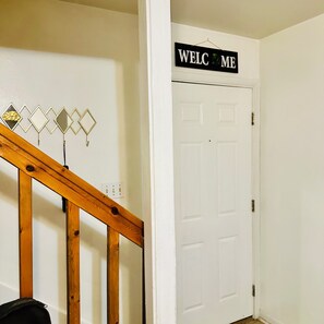 A white door with a 'WELCOME' sign above it, a wooden staircase, and a wall with decorative mirrors. - Cozy Condo 2 - Adorable 3-bedroom townhome with AC in niceville (Niceville)