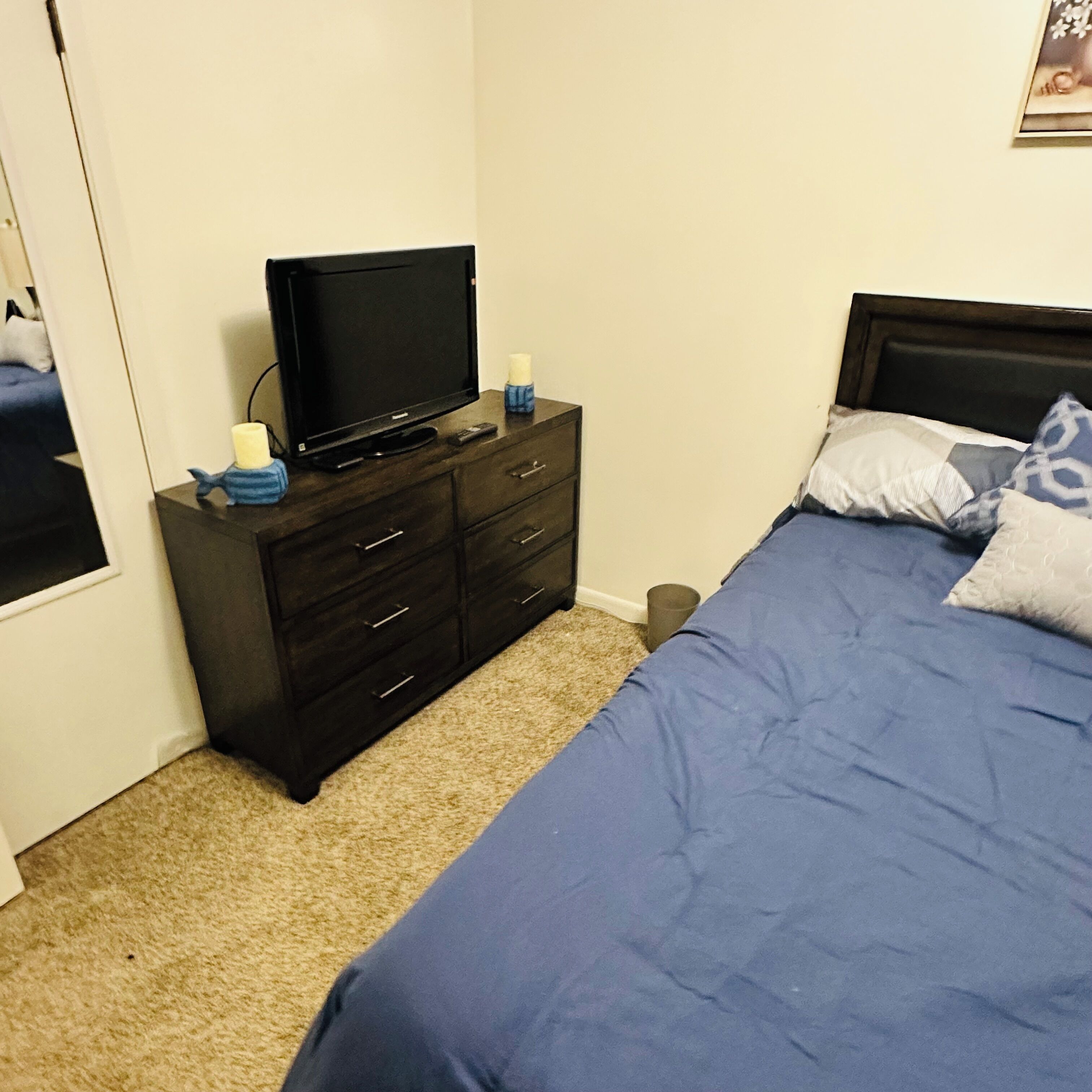Un dormitorio con cama, cómoda, televisor y una ventana pequeña.
