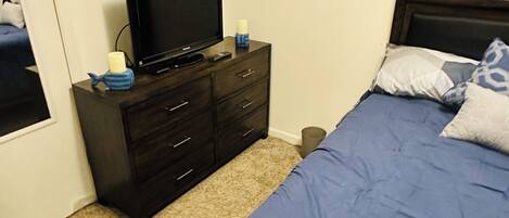 Un dormitorio con cama, cómoda, televisor y una ventana pequeña.