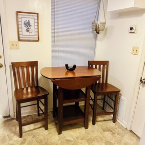 A small dining area with a wooden table and two chairs, a framed picture on the wall, and a window with blinds. - Cozy Condo 2 - Adorable 3-bedroom townhome with AC in niceville (Niceville)