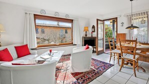 Ein Wohnzimmer mit Sofa, Sesseln, einem Couchtisch, einem Kamin und einem Essbereich mit Tisch und Stühlen.
