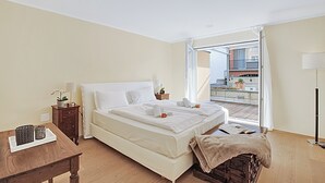 Une chambre d’hôtel comprenant un lit, une table de chevet, une lampe, une fenêtre donnant sur des immeubles et un balcon.