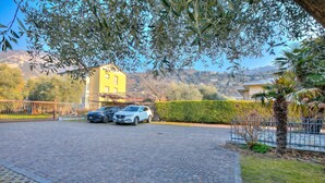 Ein gepflasterter Parkplatz mit zwei Autos, ein gelbes Gebäude im Hintergrund und ein klarer Himmel.