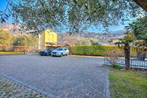 A paved parking area with two cars, a yellow building in the background, and a clear sky. - Agritur Laura- Oasi di luce 5 with Shared Garden, Torbole sul Garda, Italy (Torbole sul Garda)