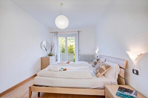 Quarto com cama de madeira, mesa de cabeceira, espelho e vista para o verde lá fora.