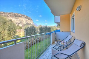 Ein Balkon mit zwei Loungesesseln, einem kleinen Tisch, einer Tasse und einem Teller, sowie Blick auf Berg und Bäume.