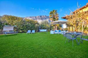A well-maintained backyard with a grassy lawn, outdoor furniture, and a view of a mountain range. - Agritur Laura- Essenza di rosa 2 with Shared Garden, Torbole sul Garda, Italy (Torbole sul Garda)
