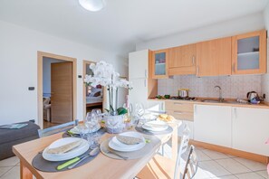 A modern kitchen with wooden cabinets, a dining table set for two, and a small dining area with a sofa. - Agritur Laura- Essenza di rosa 2 with Shared Garden, Torbole sul Garda, Italy (Torbole sul Garda)
