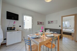 A dining area with a table set for four, a television mounted on the wall, and a kitchenette with a microwave. - Agritur Laura - Armonia Verde 1 with Shared Garden, Torbole sul Garda, Italy (Torbole sul Garda)