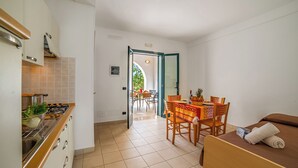 Quarto de hotel compacto com cozinha americana, área de refeições com mesa e cadeiras, e uma cama com toalha.