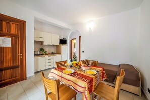 A dining area with a table set for two, a sofa, and a kitchen in the background. - Beach in 5 min | Pool Access | n.59, Otranto, Italy (Otranto)