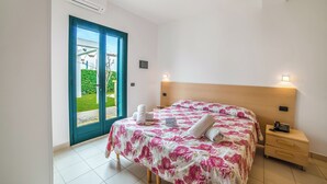 Quarto com cama, mesa de cabeceira, telefone fixado na parede e porta para uma varanda.