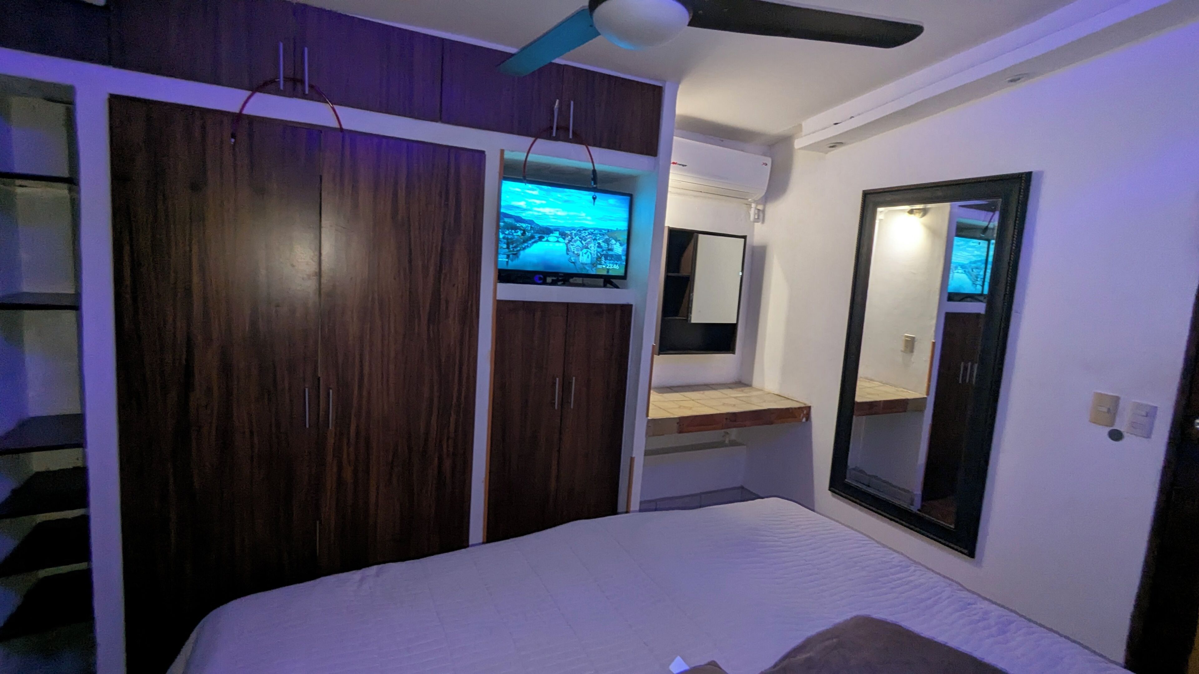 Ein Schlafzimmer mit einem Bett, einem an einer Holdecke montierten Fernseher, einem Spiegel und einem Deckenventilator.