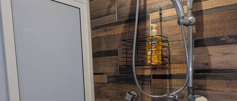 A shower with a handheld showerhead and a handheld shower attachment, a soap dispenser, and a metal rack.